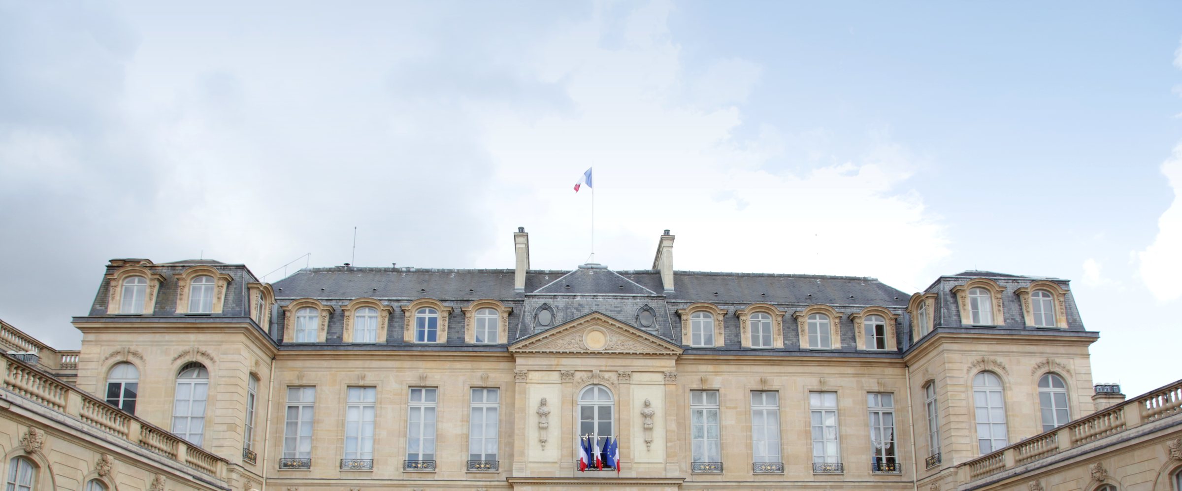 La façade du palais de l'Élysée vue de face depuis la cour d'honneur, drapeau tricolore au sommet du toit.